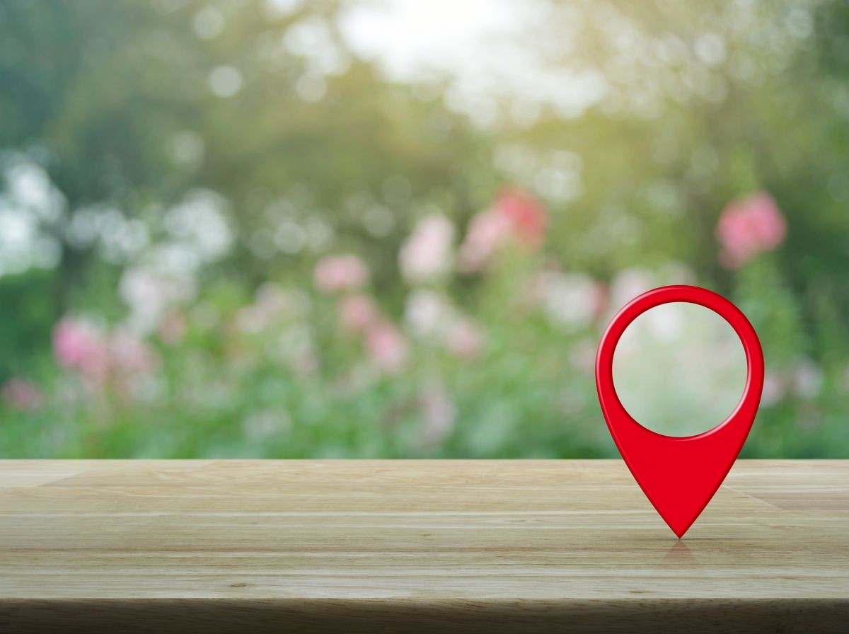 Map pin location button on wooden table over blur pink flower and tree in garden, Map pointer navigation concept